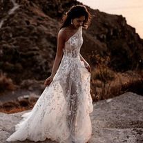 a woman in a white wedding dress walking on the beach at sunset with her back to the camera