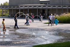 children playing in the water fountain with their parents and dads walking around it on a sunny day