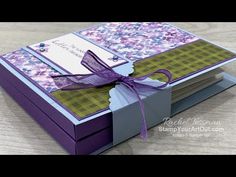 an open box with a purple ribbon tied around the top and bottom, sitting on a table