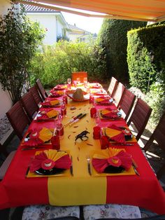 an outdoor dining area with red and yellow table cloths, place settings and utensils