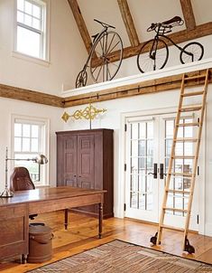 a room with a ladder, desk and bike mounted to the wall over it's door