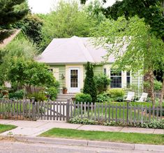 a small green house surrounded by greenery and trees on a sunny day in the suburbs