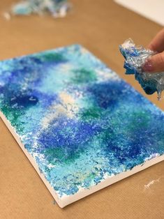 a person is painting on a piece of cardboard with blue and green paint over it