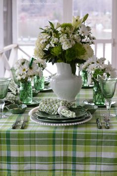 the table is set with green and white dishes, silverware, and flowers in vases