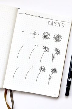 an open notebook with daisies drawn on it next to a black marker and pen