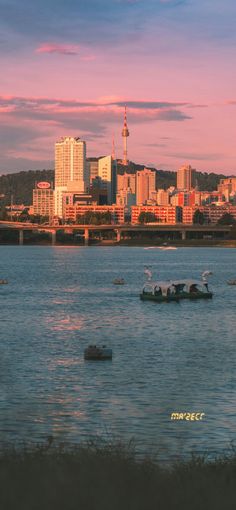 some boats are out in the water with buildings in the background and a pink sky