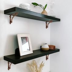 two black shelves with pictures and vases on them in a white walled bathroom area