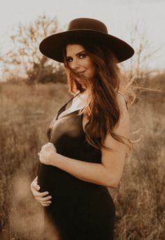 a pregnant woman in a black dress and hat poses for a photo while wearing a wide brimmed hat