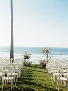 rows of white chairs sitting on top of a lush green field next to the ocean