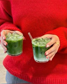 a woman in red sweater holding two glasses filled with green smoothie