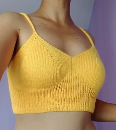 a woman in a yellow bra top is holding her hand out to the side while standing against a purple wall