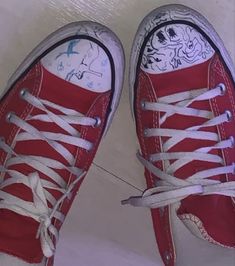 two red converse shoes with white laces on the bottom and one has a cartoon character painted on it