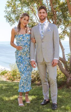 a man and woman standing next to each other in front of a tree with the ocean behind them