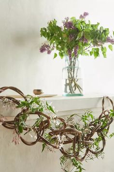 a vase filled with purple flowers sitting on top of a white shelf next to a plant