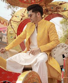 a man in yellow jacket and white pants sitting on top of a horse drawn carriage