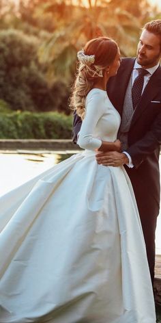 a bride and groom standing next to each other in front of a body of water