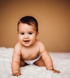 a baby laying on top of a white bed next to a brown wall and wearing a diaper