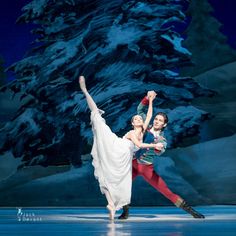 two people are performing on the ice in front of a christmas tree and snow covered mountain