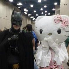 two people dressed up as hello kitty and batman in an indoor convention hall, one wearing a cat costume