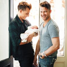 a man holding a baby while standing next to another man in front of a door