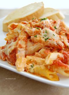 a white plate topped with pasta covered in sauce and cheese next to french bread on a table