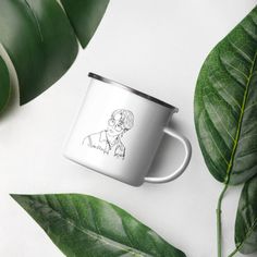 a white coffee mug with a drawing of a man on it next to green leaves