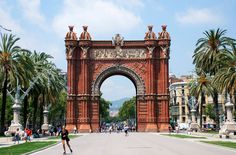 people are walking around in front of an ornate gate with palm trees on either side