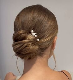 a woman with her hair in a low bun and two small pearls on the back of her head