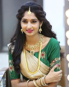 a woman in a green and white sari with gold jewelry on her neck, smiling at the camera