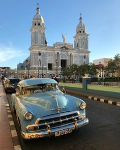 an old blue car parked in front of a large white building with two steeples