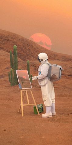 a man in white suit painting on an easel next to a desert landscape with cacti