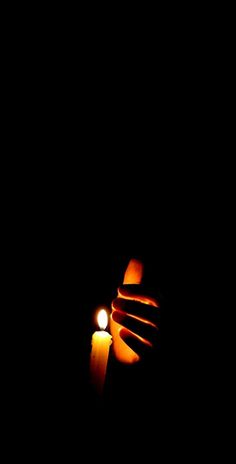 a person holding a lit candle in the dark with their hand on top of it