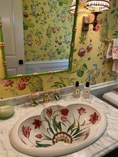 a bathroom sink sitting under a mirror in front of a green wallpapered wall