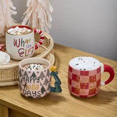 three coffee mugs sitting on top of a wooden table next to christmas trees and marshmallows