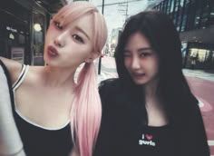 two young women standing next to each other on a city street with buildings in the background