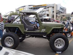 a green jeep parked on top of a parking lot next to other cars and people