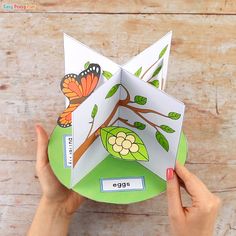 someone is holding an origami tree with leaves and butterflies on it, in front of a wooden background