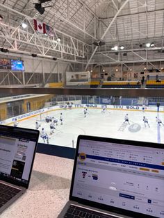 two laptops sitting on top of a table in front of an ice rink with people playing hockey