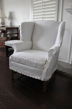 a white chair sitting on top of a wooden floor next to a lamp and window