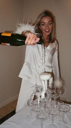 a woman pouring champagne into wine glasses on top of a white tablecloth covered table