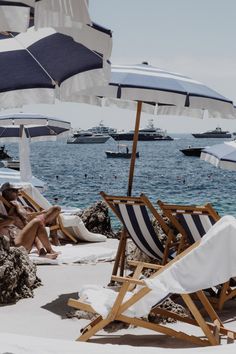 people lounging on the beach under umbrellas and boats in the water behind them