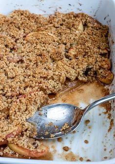 an apple crisp dessert in a white casserole dish with a spoon resting on it