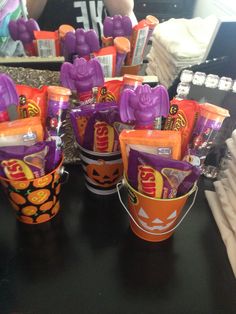 there are many halloween candy in cups on the table with orange and purple candies