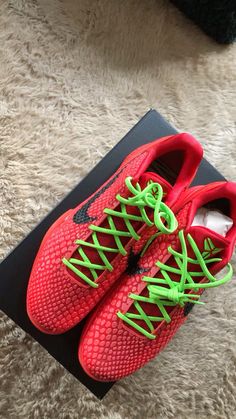 a pair of red and green shoes sitting on top of a black shoe box next to a white rug