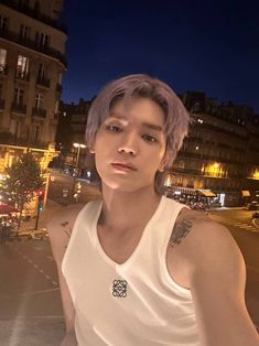 a man with grey hair standing in front of a street at night wearing a white tank top