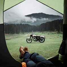 a man laying in a tent with his feet on the ground next to a motorcycle