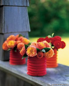 three red vases with yellow and orange flowers in them on a wooden ledge outside