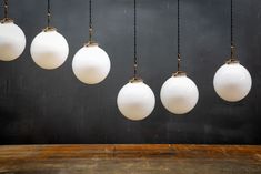 five white light bulbs hanging from a wooden table with black wall in the back ground