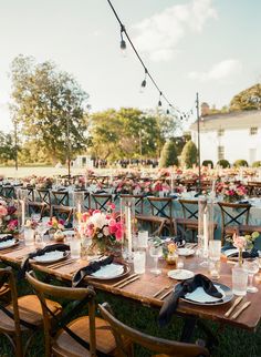 a table set up with plates and glasses for an outdoor wedding reception in the grass