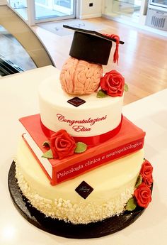 a three tiered cake decorated with books and a graduation cap on top is sitting on a table